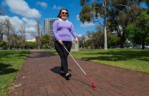 A person walking down a path outside using their cane.