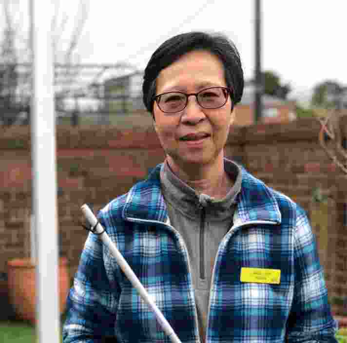 A person standing outside smiling at the camera while holding their white cane.