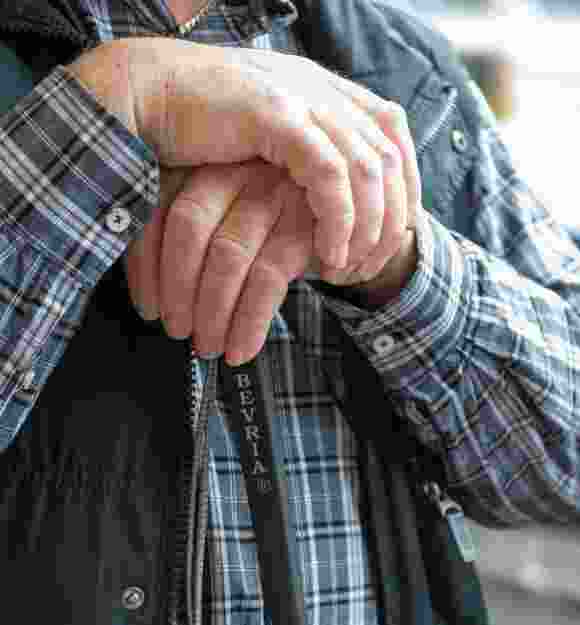 Close up of two hands resting on the top of a white cane.