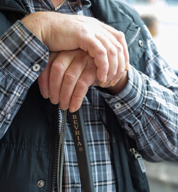 Close up of two hands resting on the top of a white cane.