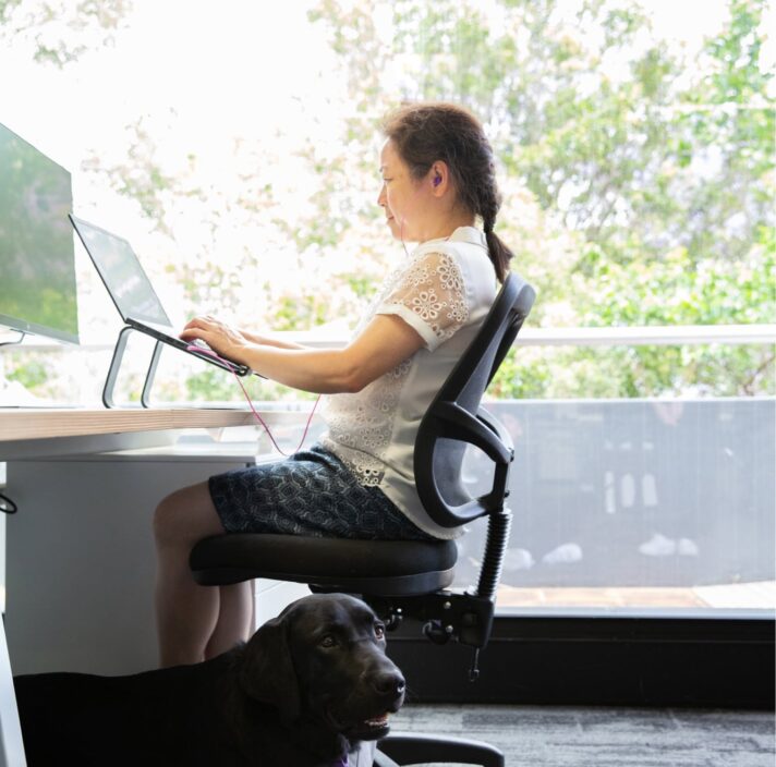 A person sitting at a desk using their laptop. The image is a profile view.