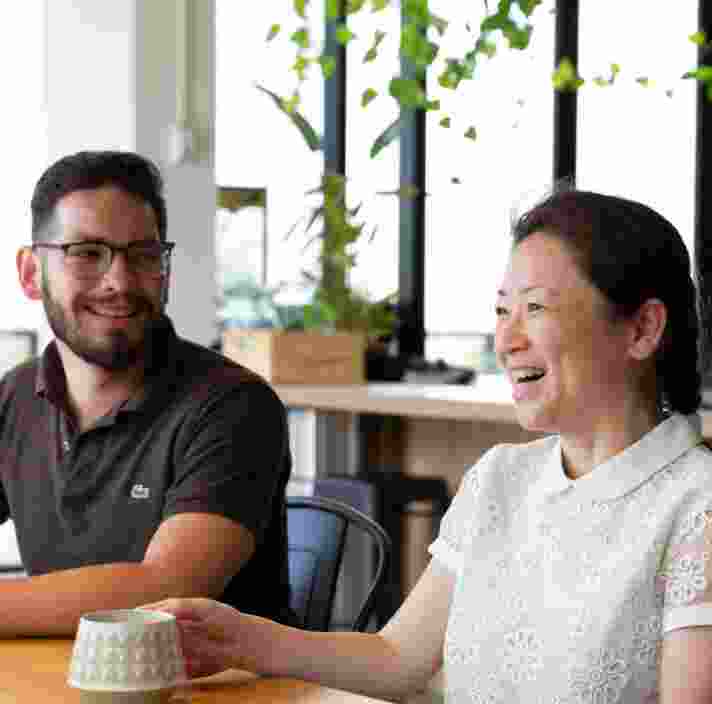 Two people sitting at cafe table. Both people are smiling.