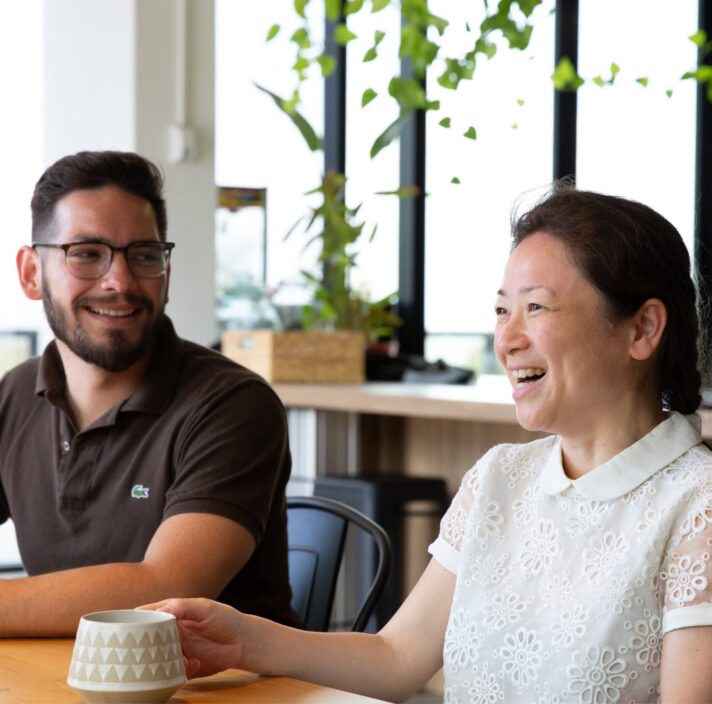Two people sitting at cafe table. Both people are smiling.
