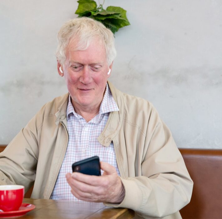 An older adult man sitting at a cafe looking at their phone.