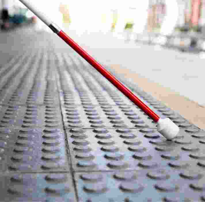 Close up image of the bottom half of a white cane on tactile tiles.