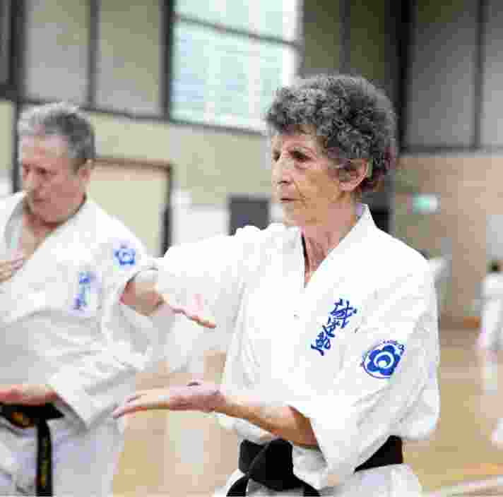 Two people at an indoor karate class. Both are in a karate uniform and are holding their hands in a karate pose.