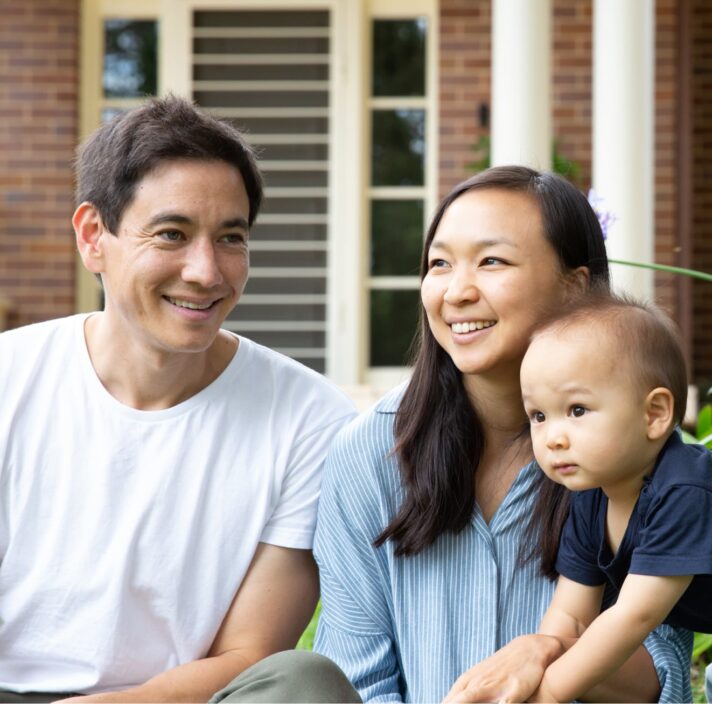 A mother and father sitting outside watching their baby play.