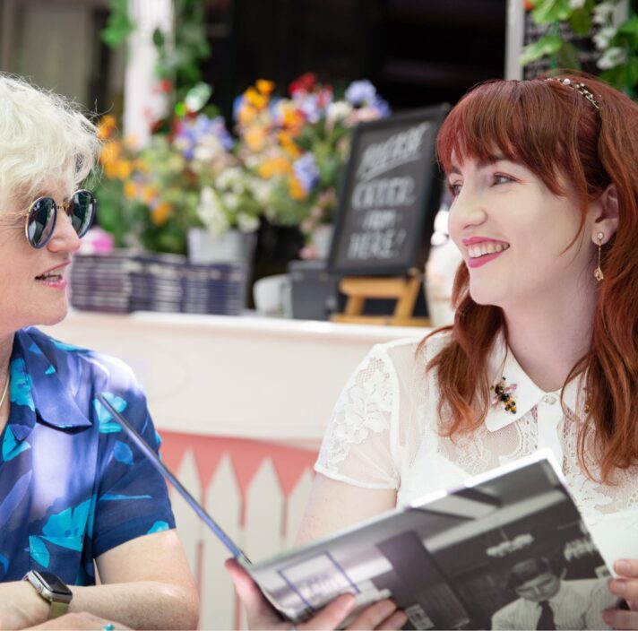 Two people sitting at a cafe looking at each other. They are both smiling and one is holding a menu.