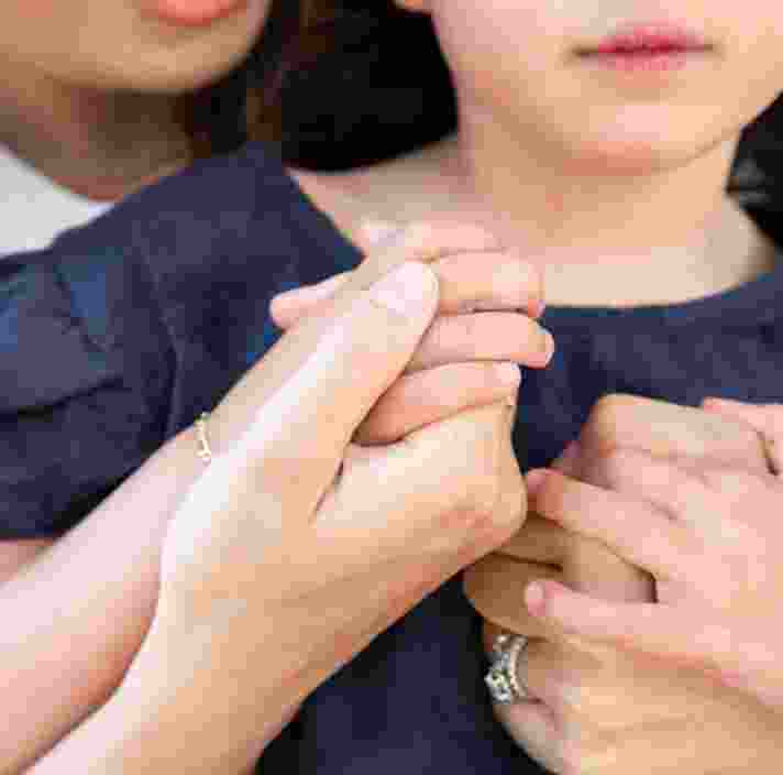 A close up of a mother cuddling a young child from behind, their hands are embraced.