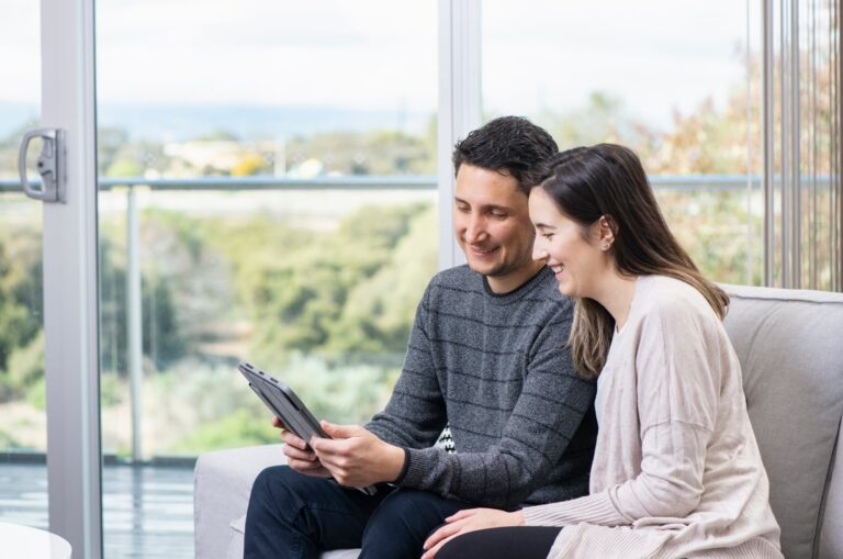 Two people sitting on a couch looking at a tablet together