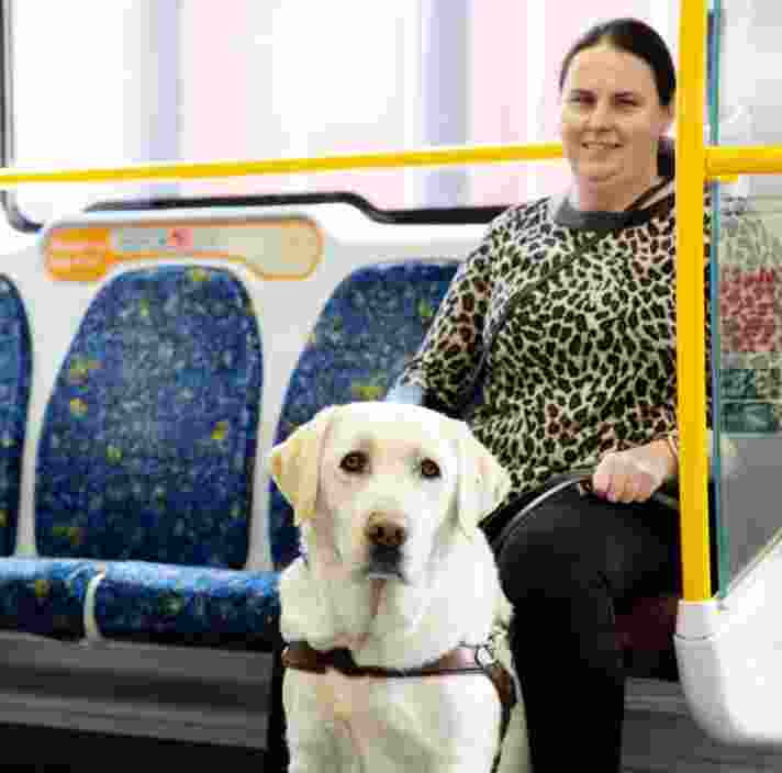 Nicole sitting on a train seat with Guide dog Toby sitting in front of her