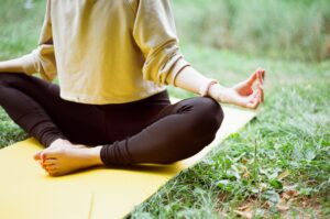 a person practicing yoga, sitting on a yellow mat outdoors