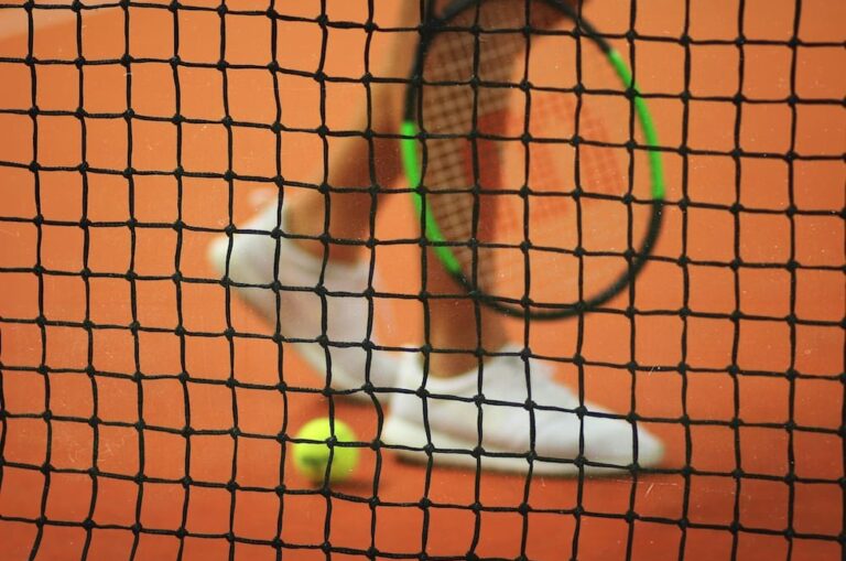 image of a tennis net, with a players legs and tennis racket visible through the net