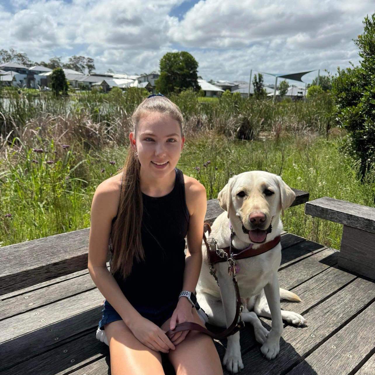 Karlee sits next to her yellow Guide Dog in harness