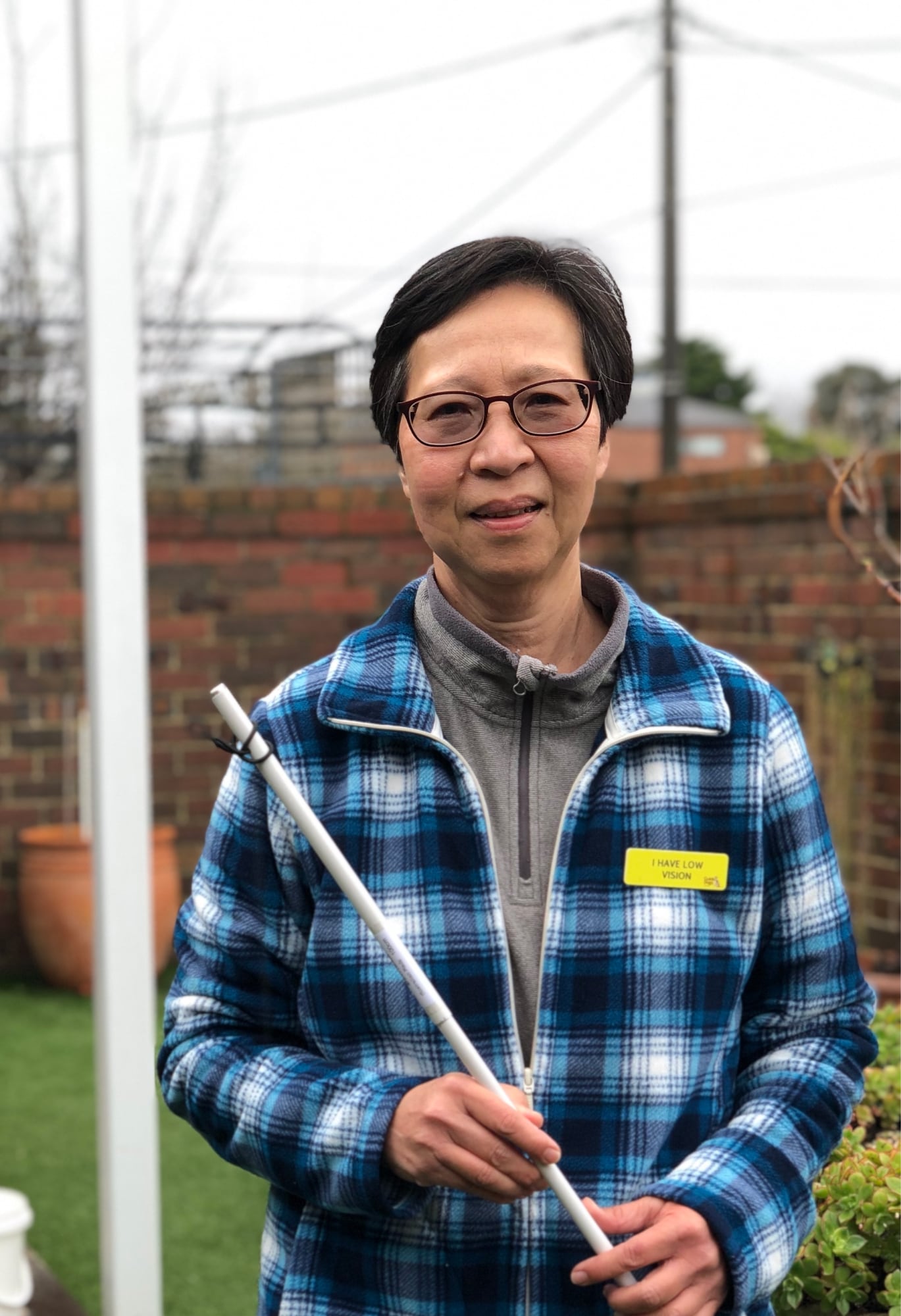 A person standing outside smiling at the camera while holding their white cane.