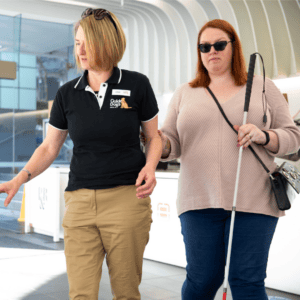 A Guide Dogs staff member assisting a person with a cane.