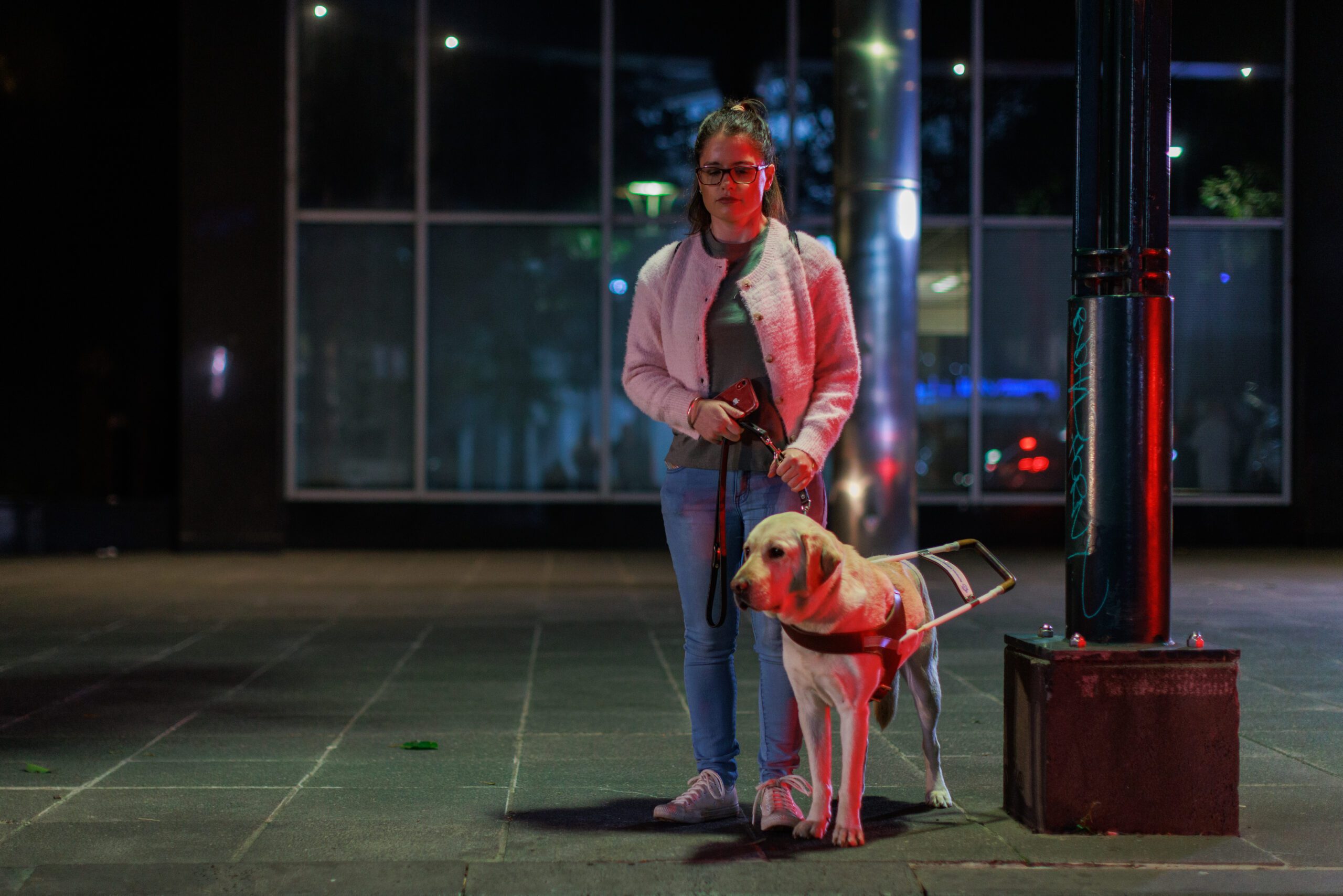 Emma stands on a dark street with her yellow Labrador Guide Dog