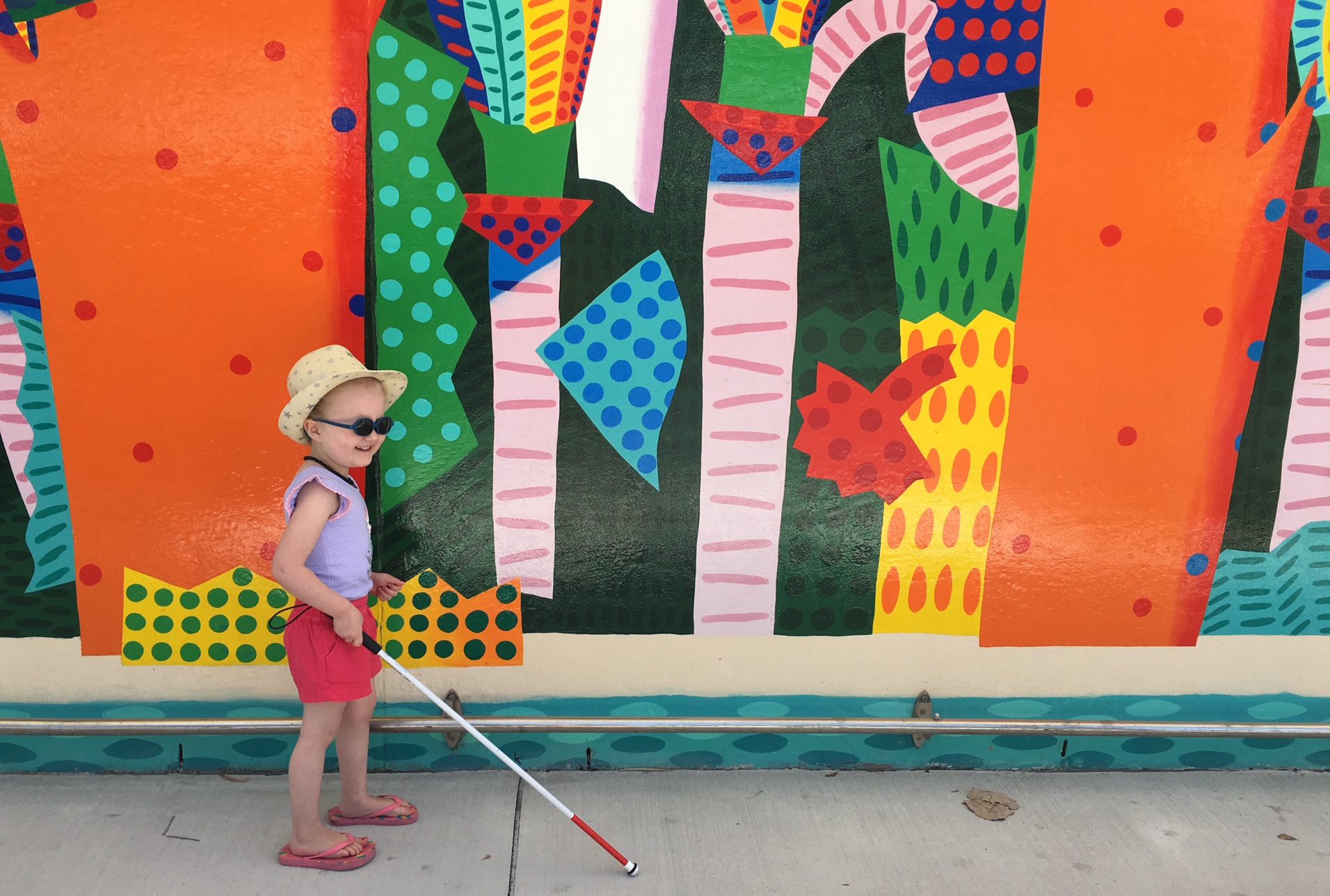 Stella holding her cane in front of a colourful mural