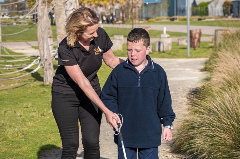 A Guide Dogs staff member assists a child using a white cane