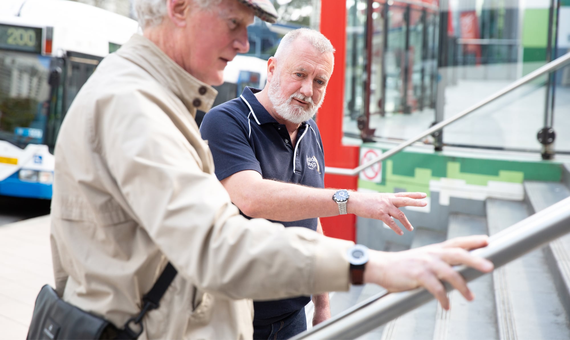 A Guide Dogs staff member assisting an an older adult with navigating a handrail.
