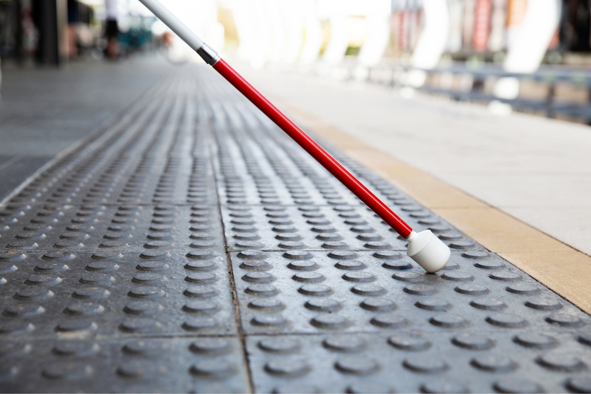 Close up image of the bottom half of a white cane on tactile tiles.