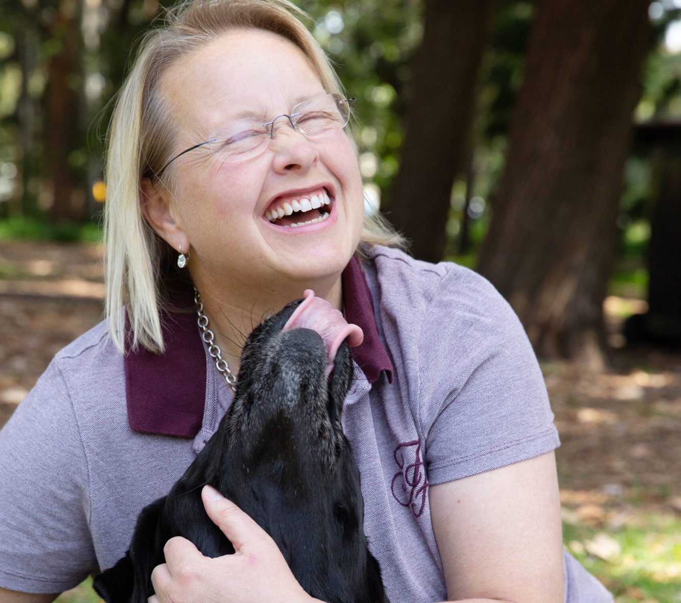A person laughs as their black Labrador Guide Dog licks their face.