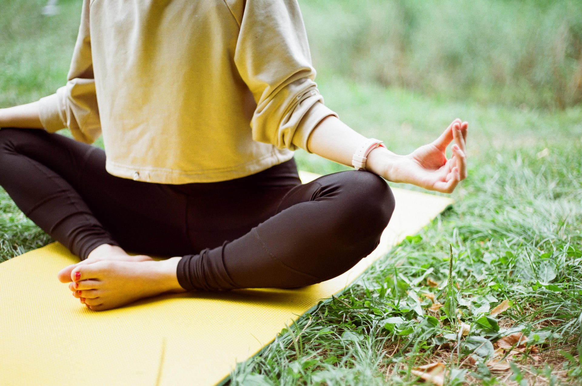 a person practicing yoga, sitting on a yellow mat outdoors